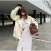 Model wearing an ivory cropped satin trench jacket with a black turtleneck.