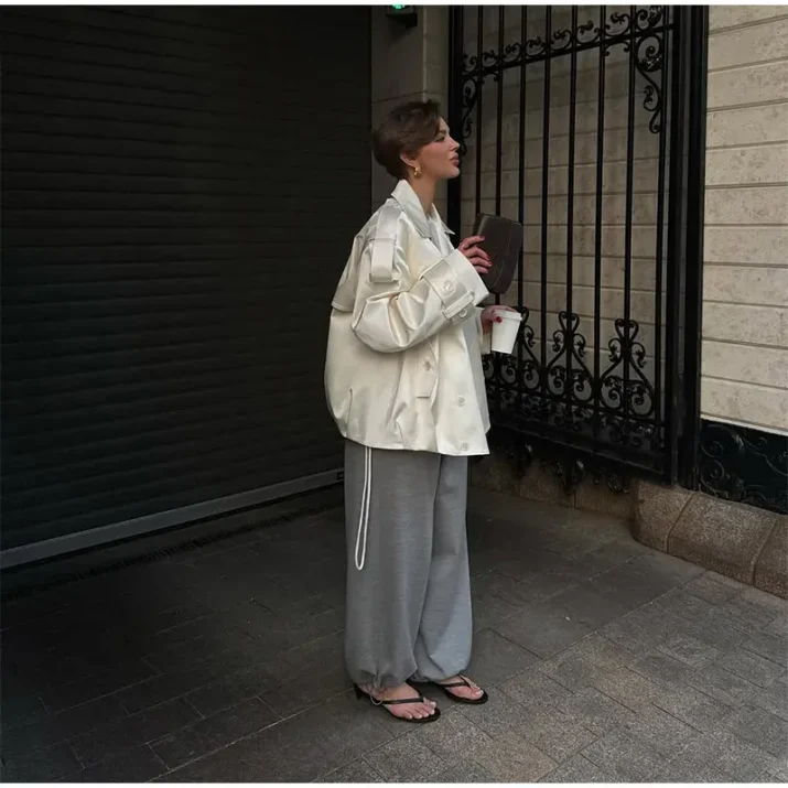 Model wearing an ivory cropped satin trench jacket with a black turtleneck.