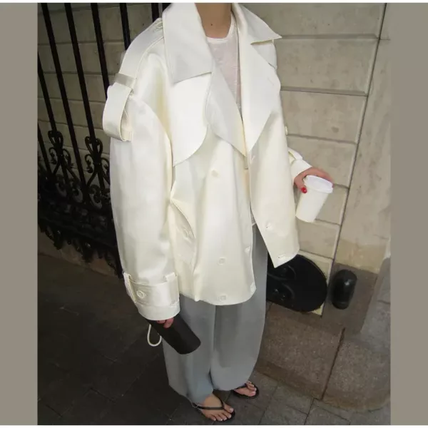 Model wearing an ivory cropped satin trench jacket with a black turtleneck.