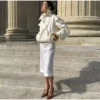 Model wearing an ivory cropped satin trench jacket with a black turtleneck.