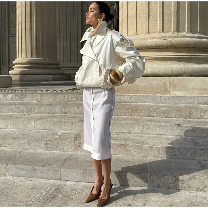 Model wearing an ivory cropped satin trench jacket with a black turtleneck.