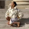 Model wearing an ivory cropped satin trench jacket with a black turtleneck.
