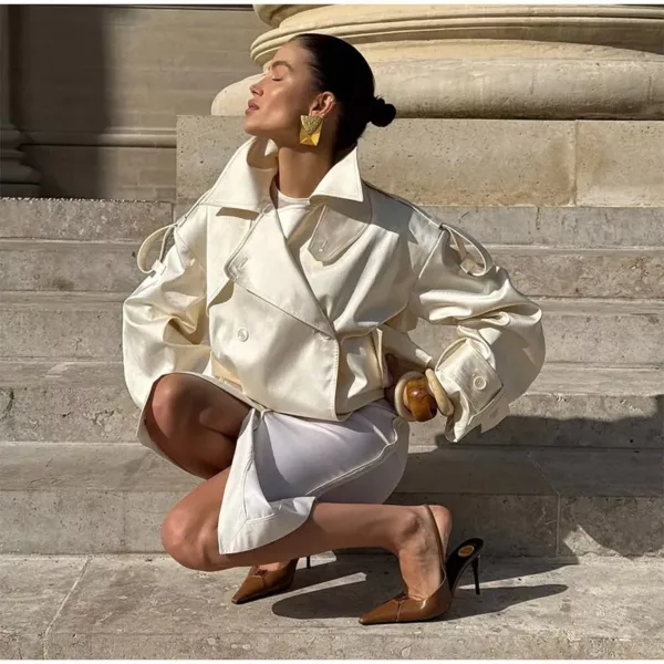Model wearing an ivory cropped satin trench jacket with a black turtleneck.