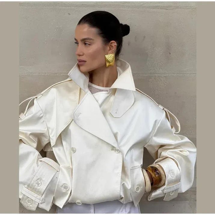Model wearing an ivory cropped satin trench jacket with a black turtleneck.