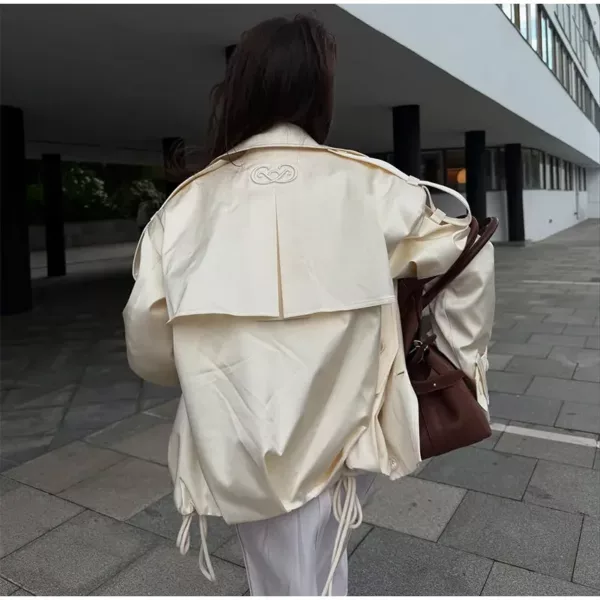 Model wearing an ivory cropped satin trench jacket with a black turtleneck.