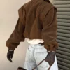 Model wearing a cropped suede bomber jacket with puff sleeves in a rich brown color