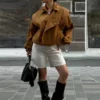 Model wearing a cropped suede bomber jacket with puff sleeves in a rich camel color
